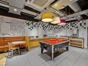 A billiards table in a room with a pool table, a brown leather booth, and a counter with a coffee machine.