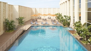 Zona de piscina con sillas de descanso y sombrillas, rodeada por un muro alto con paneles decorativos.