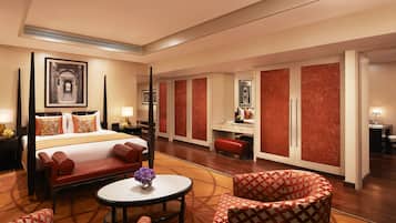 Quarto de hotel com uma cama de dossel, um espaço de estar com uma mesa redonda e cadeiras, uma escrivaninha com cadeira e um guarda-roupa com portas espelhadas.