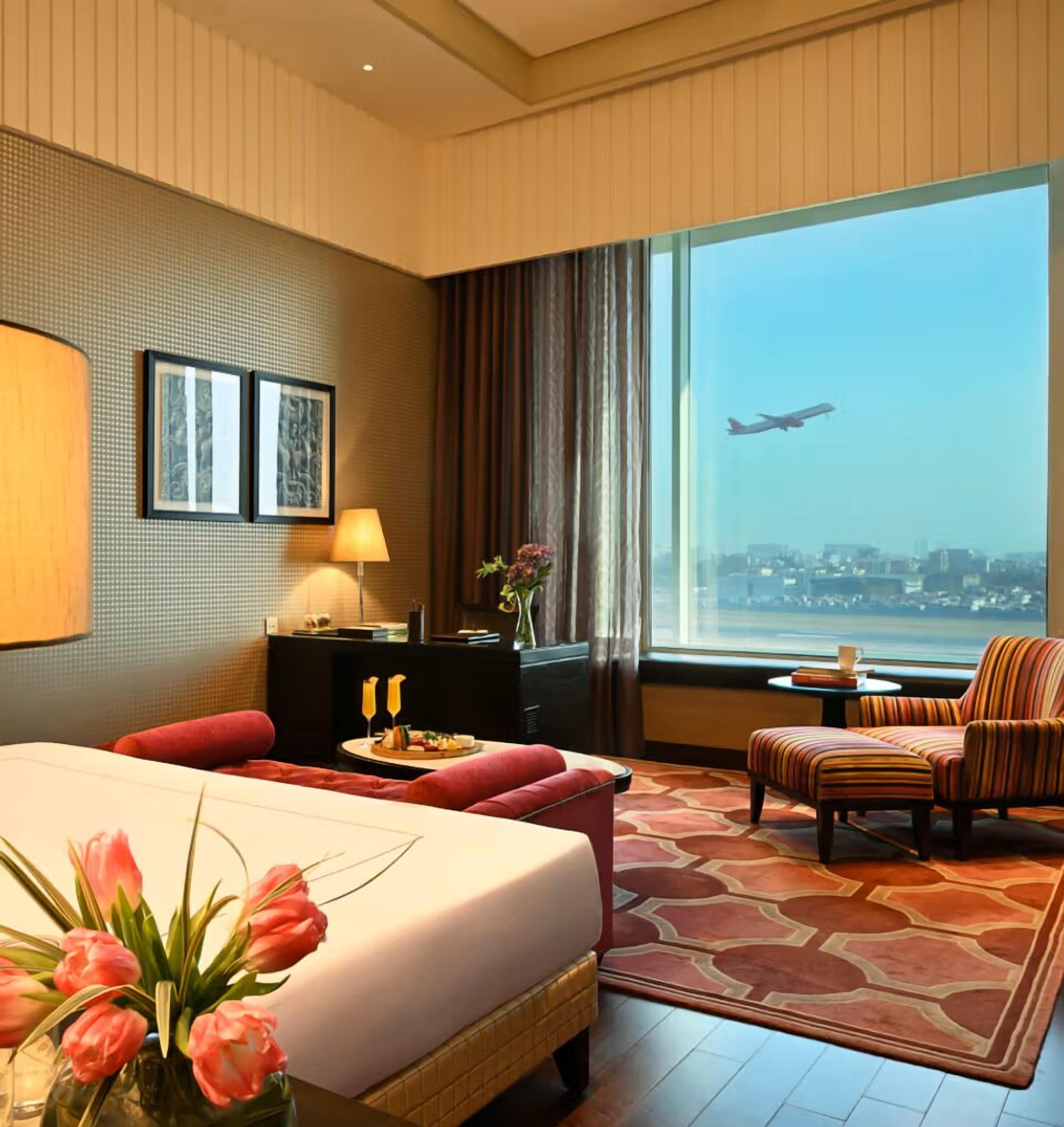 Une chambre d’hôtel avec un lit, un bureau, une chaise, une vue sur un avion et un panorama sur la ville.