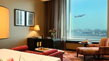Une chambre d’hôtel avec un lit, un bureau, une chaise, une vue sur un avion et un panorama sur la ville.