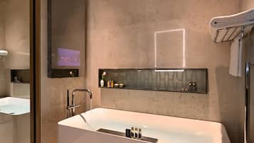 A modern bathroom with a large bathtub, a mirror, and a shelf with toiletries.