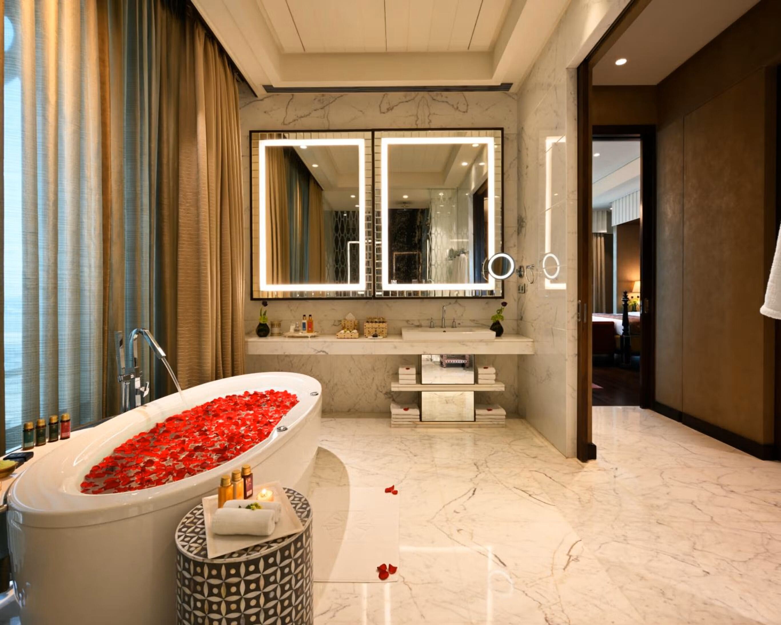 A modern bathroom with a large bathtub filled with rose petals, a vanity with a mirror, and marble flooring.