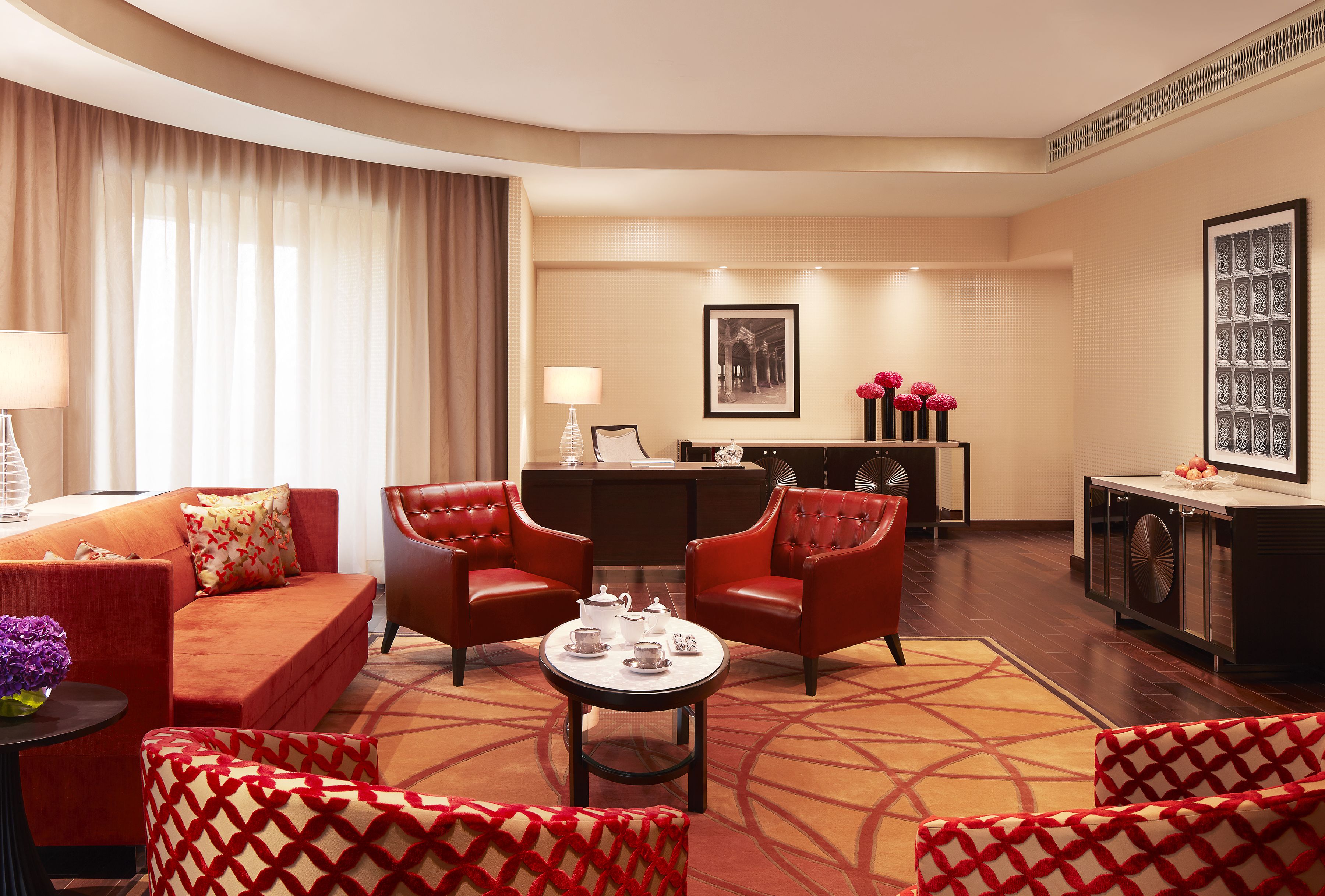 Une chambre d’hôtel avec un canapé rouge, deux fauteuils rouges, une table basse et un coin repas comprenant une table et des chaises.