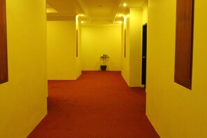 A hallway with yellow walls and a red carpet, leading to a door at the end. - Sepinggan Hotel (Balikpapan)
