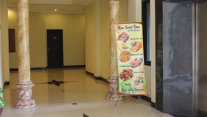 A hotel lobby with marble columns, a polished floor, and a menu stand displaying food options. - Sepinggan Hotel (Balikpapan)