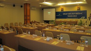 A conference room with multiple tables, chairs, and a projector screen displaying a presentation. - Sepinggan Hotel (Balikpapan)