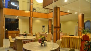 A hotel dining area with round tables, chairs, and a buffet counter. - Sepinggan Hotel (Balikpapan)