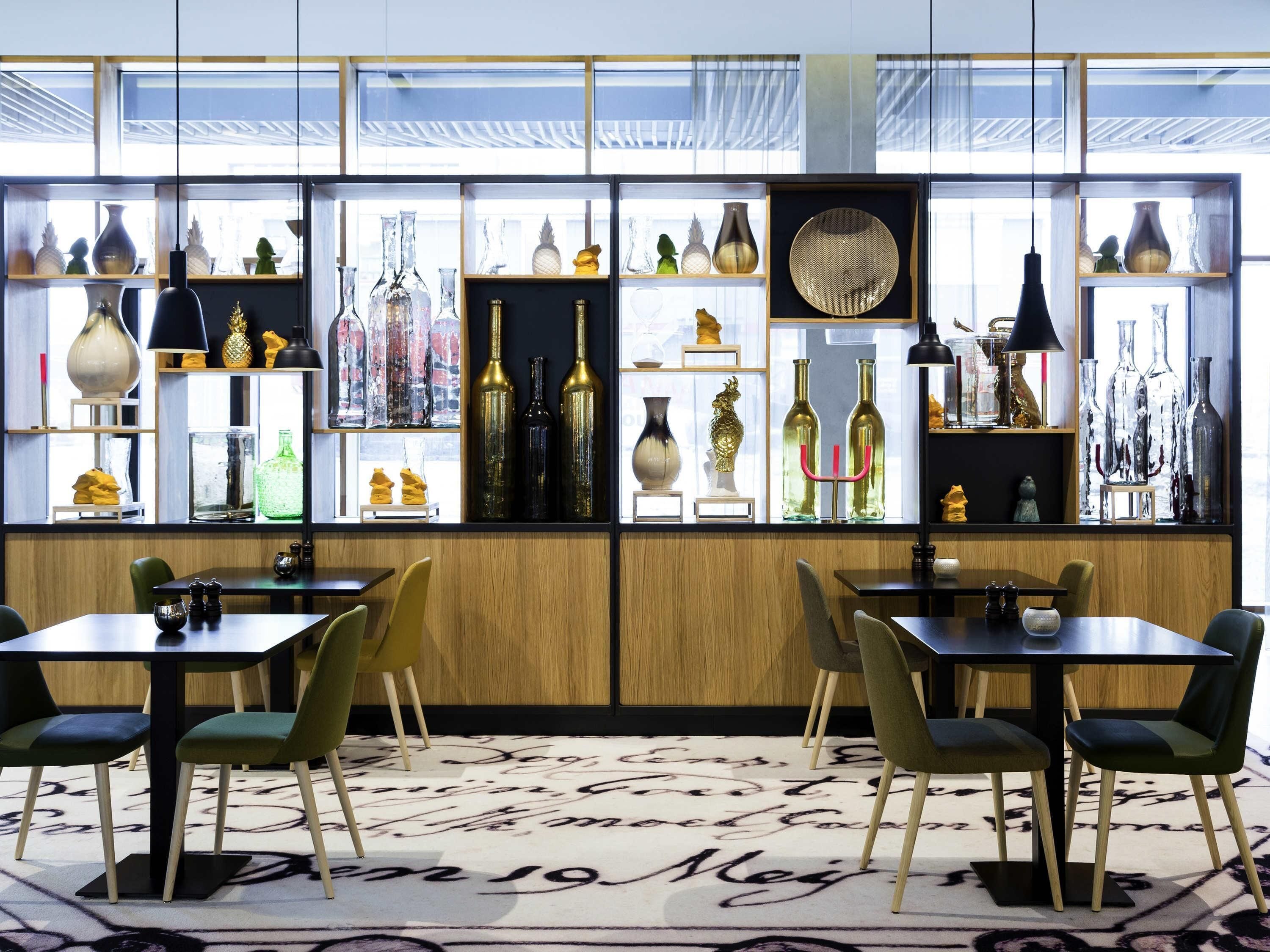 Un restaurante con una decoración moderna, que presenta paneles de madera, estanterías de vidrio y sillas tapizadas en verde.