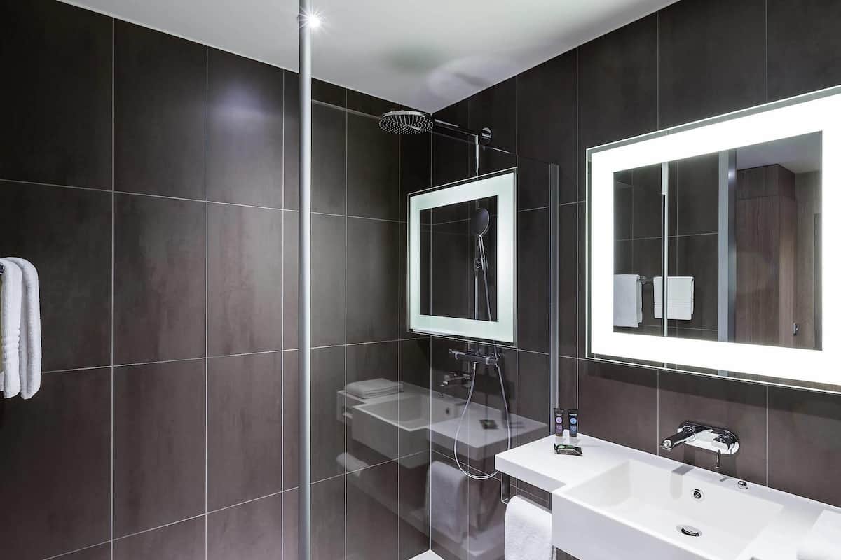 A modern bathroom with dark tiles, a glass-enclosed shower, a large mirror, and a white vanity.