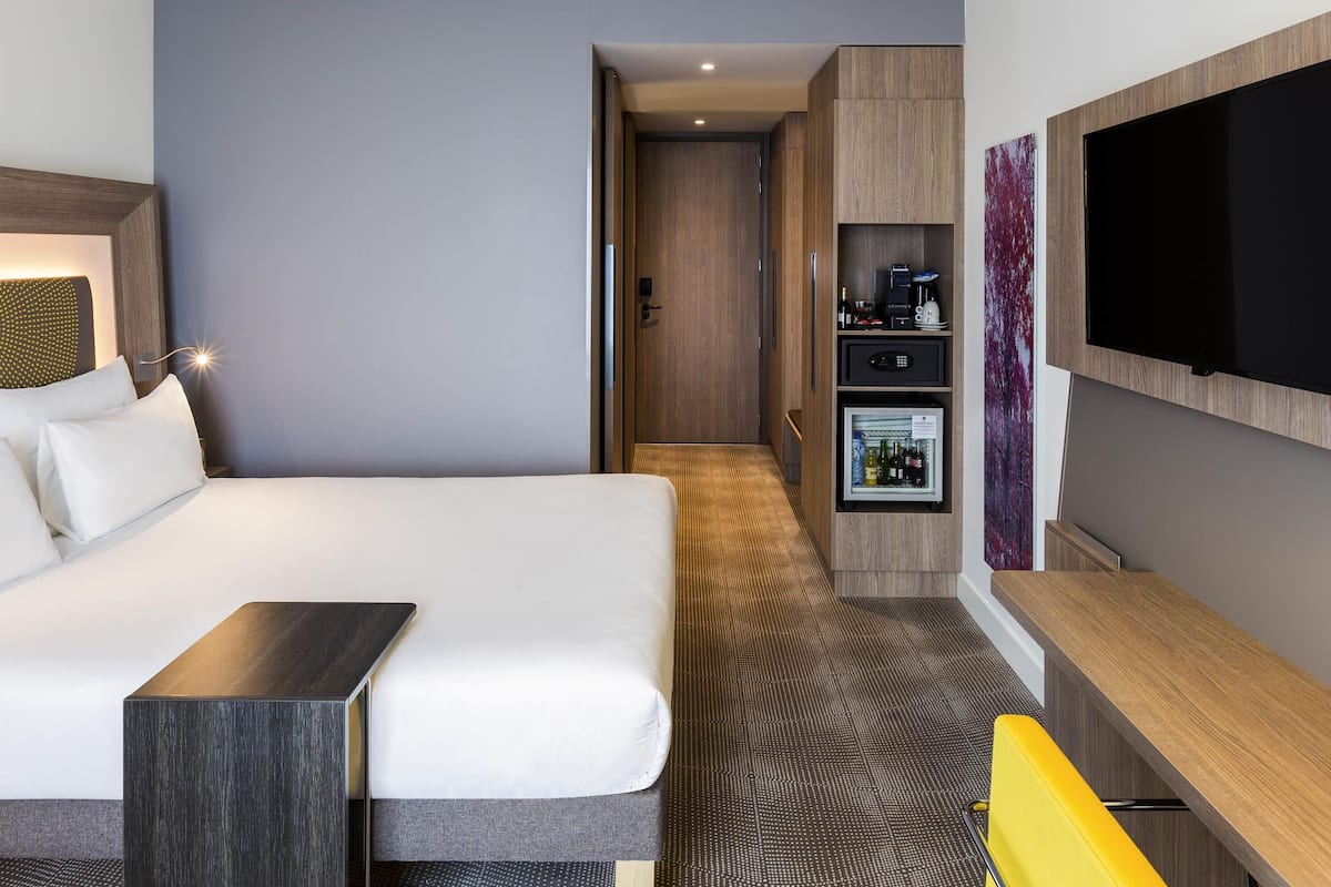 Una habitación de hotel moderna con una cama grande, un escritorio, un televisor de pantalla plana, un minibar y un vestidor.
