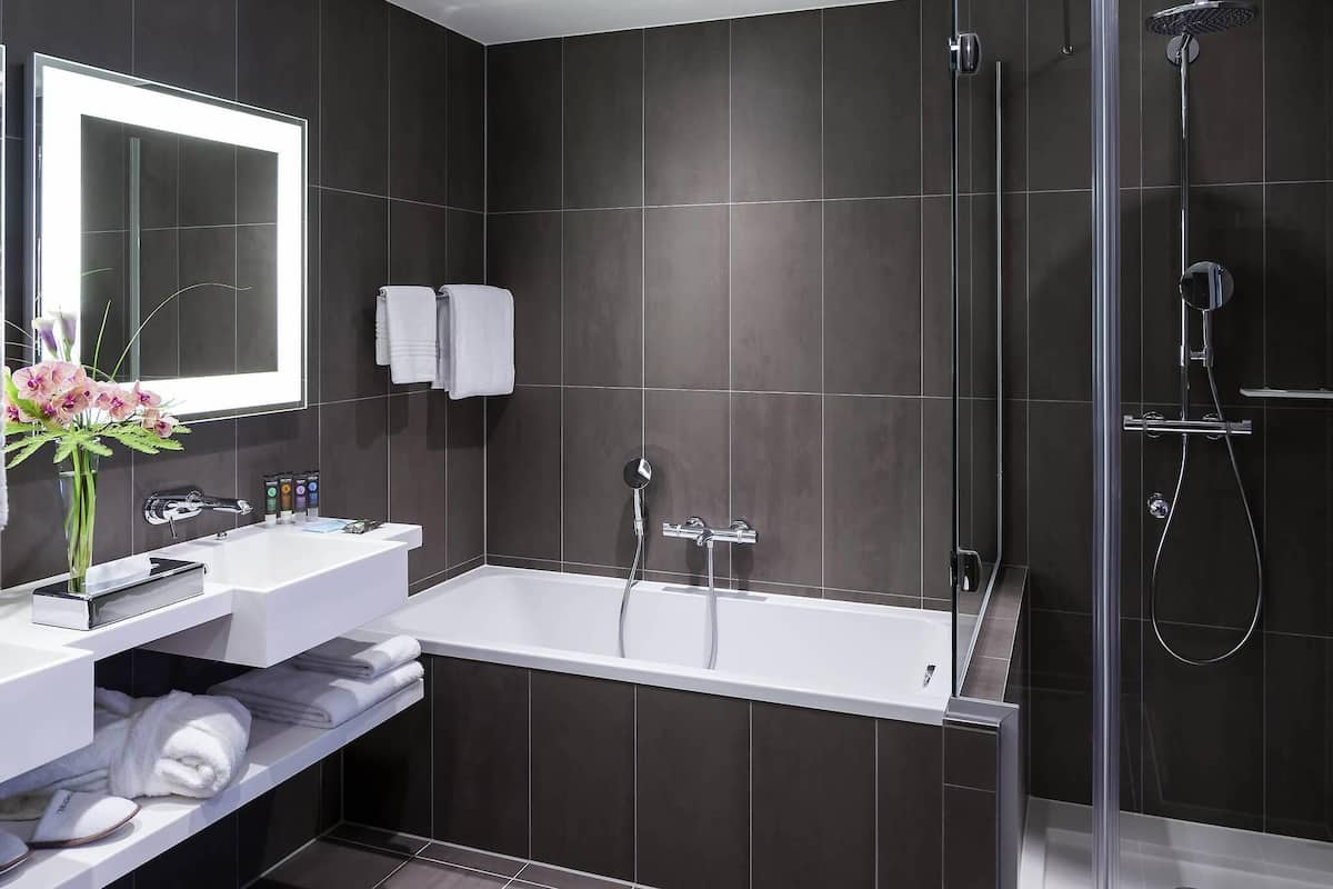 Un baño moderno con una bañera, ducha con mampara de vidrio, tocador con espejo y un florero con flores.