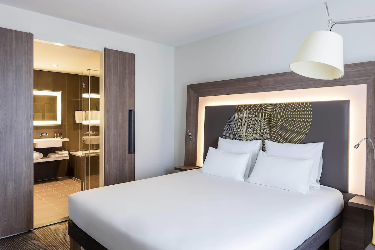 Habitación de hotel con una cama grande, baño con espejo y lavamanos, y vestidor.