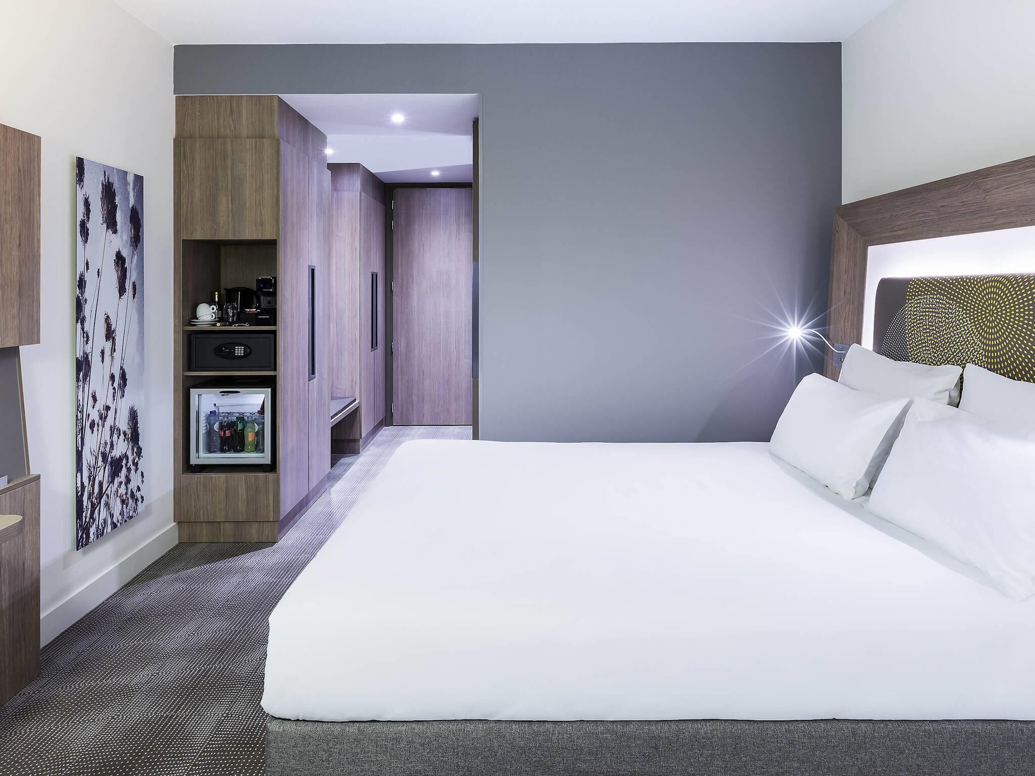 Een moderne hotelkamer met een groot bed, een kledingkast, een zithoekje en een televisie aan de muur.