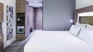 Een moderne hotelkamer met een groot bed, een kledingkast, een zithoekje en een televisie aan de muur.