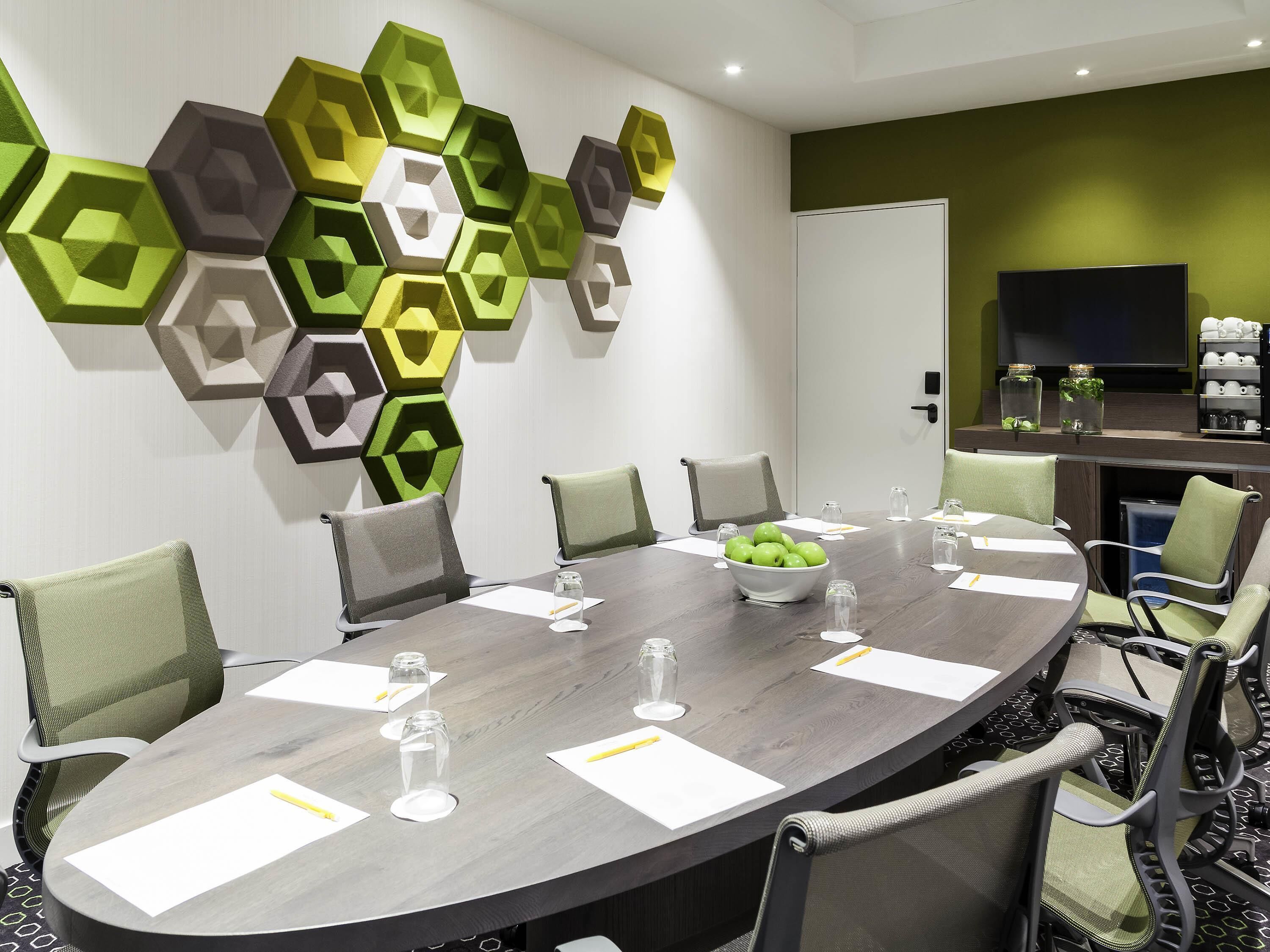 Une salle de conférence équipée d’une table ronde, de chaises, d’un téléviseur fixé au mur et d’un élément décoratif géométrique sur le mur.