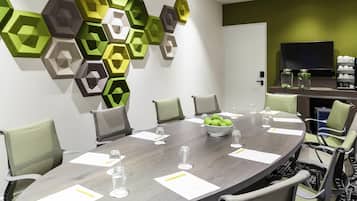 Une salle de conférence équipée d’une table ronde, de chaises, d’un téléviseur fixé au mur et d’un élément décoratif géométrique sur le mur.