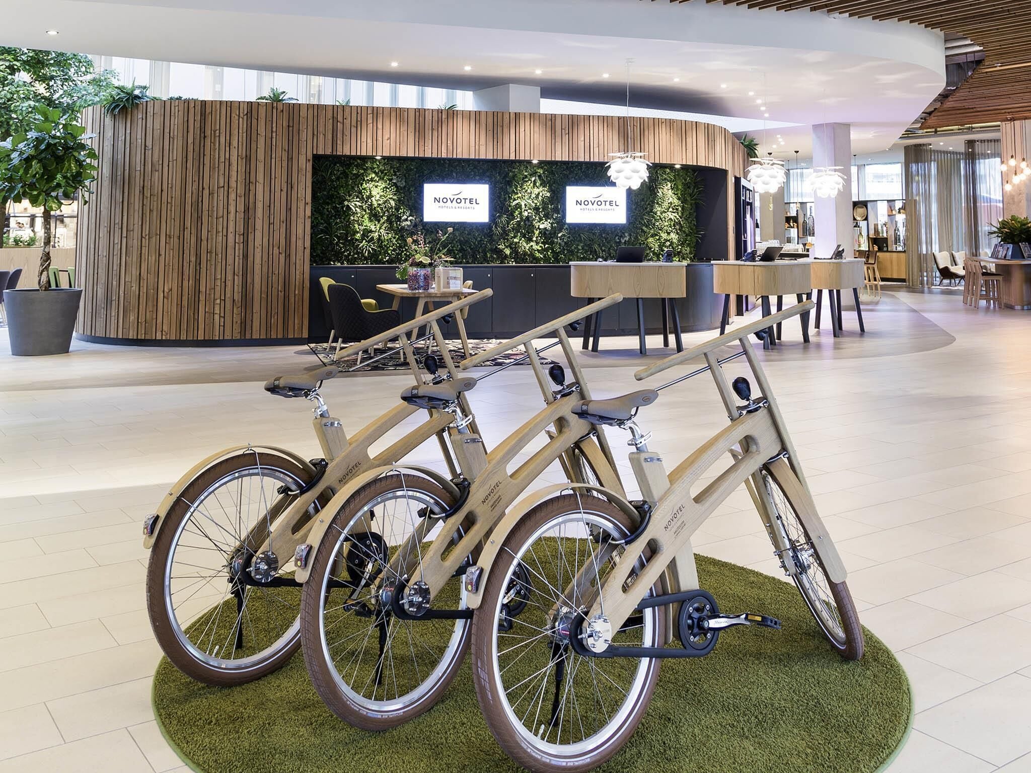 Un área de recepción con un mostrador de madera, una pared verde con plantas y tres bicicletas estacionadas al frente.