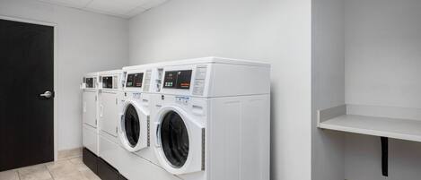 A laundry room with three stacked front-loading washing machines, a black door, and a white shelf.