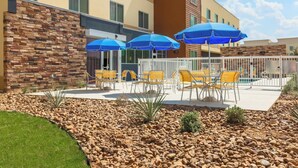 A hotel patio with outdoor seating, a pool, and a stone wall.