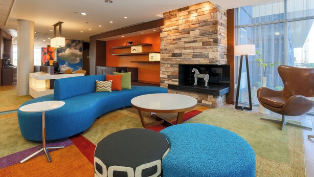 A modern hotel lobby with a blue sofa, round tables, a stone fireplace, and a large window providing a view outside.