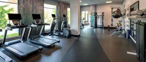 Une salle de sport équipée de tapis de course, de vélos elliptiques et de matériel de musculation.