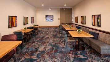 A hotel room with a carpeted floor, multiple seating options including tables and sofas, and artwork on the walls.