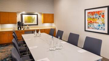 A conference room with a long table, chairs, a coffee maker, and a framed abstract painting on the wall.