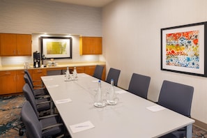 Una sala de conferencias con una mesa larga, sillas, una cafetera y un cuadro abstracto enmarcado en la pared.