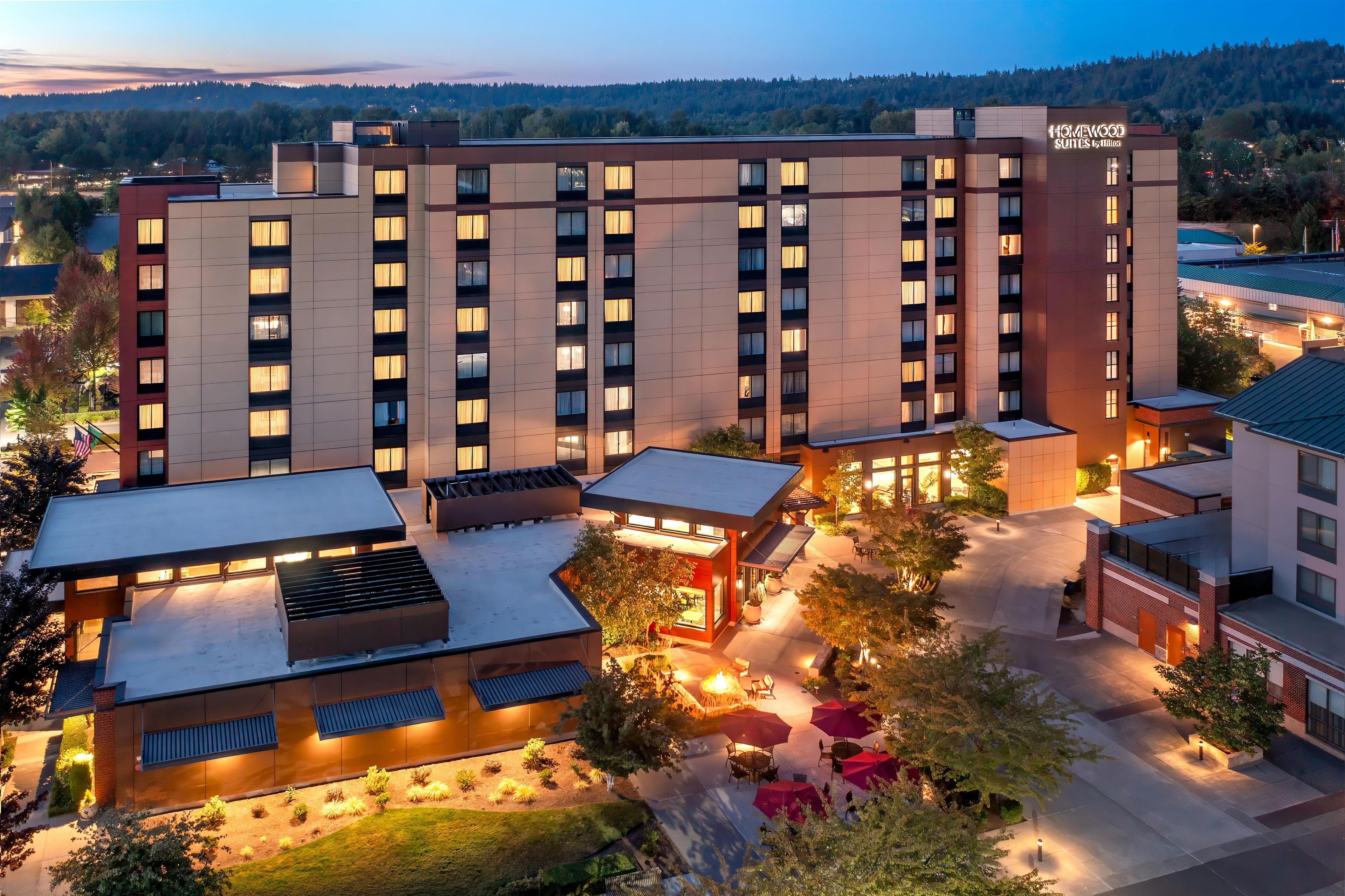 Un hotel de varios pisos con techo plano, zona de estar al aire libre y vistas a un área boscosa.