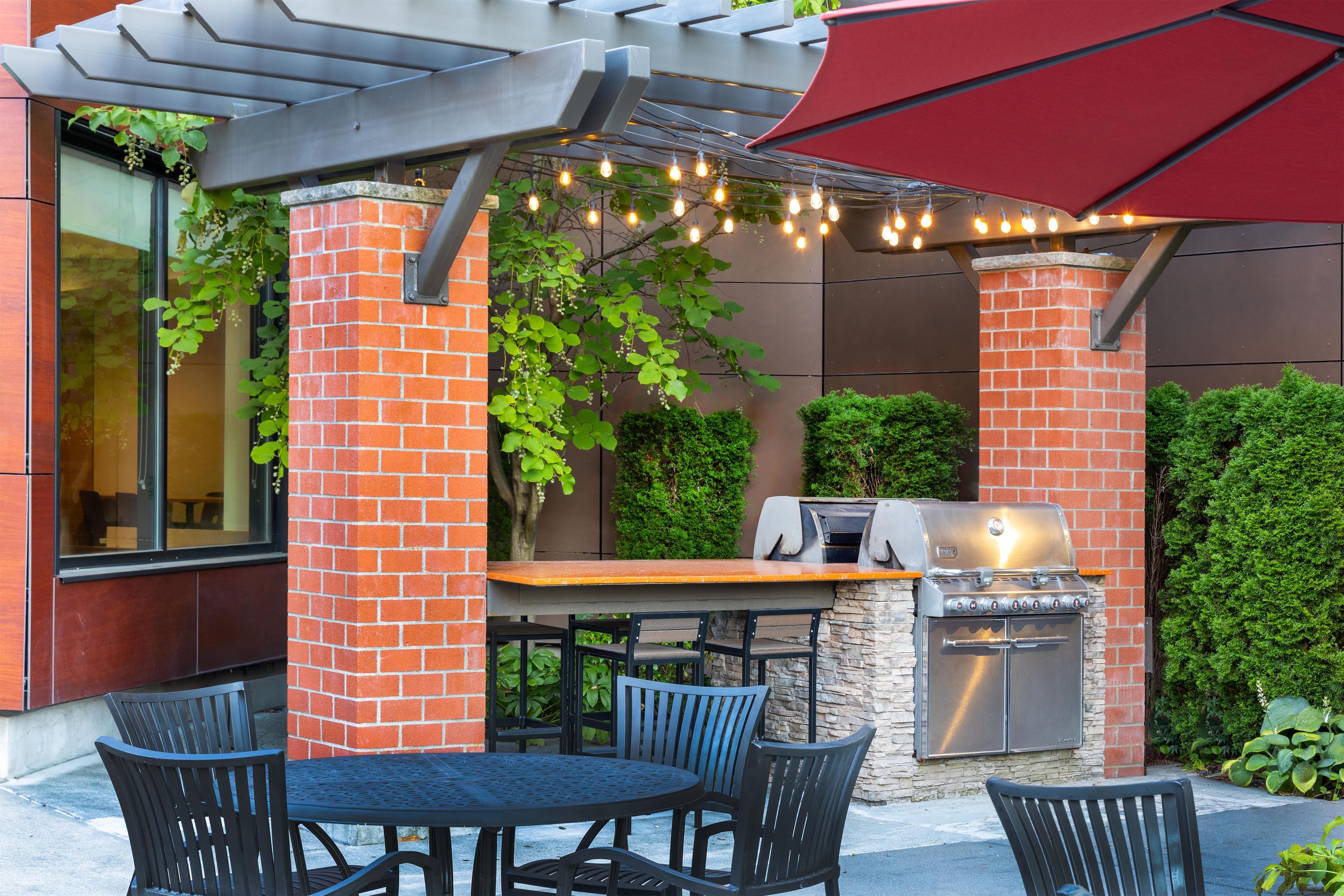 Une terrasse extérieure avec une colonne en briques, un barbecue et des guirlandes lumineuses.
