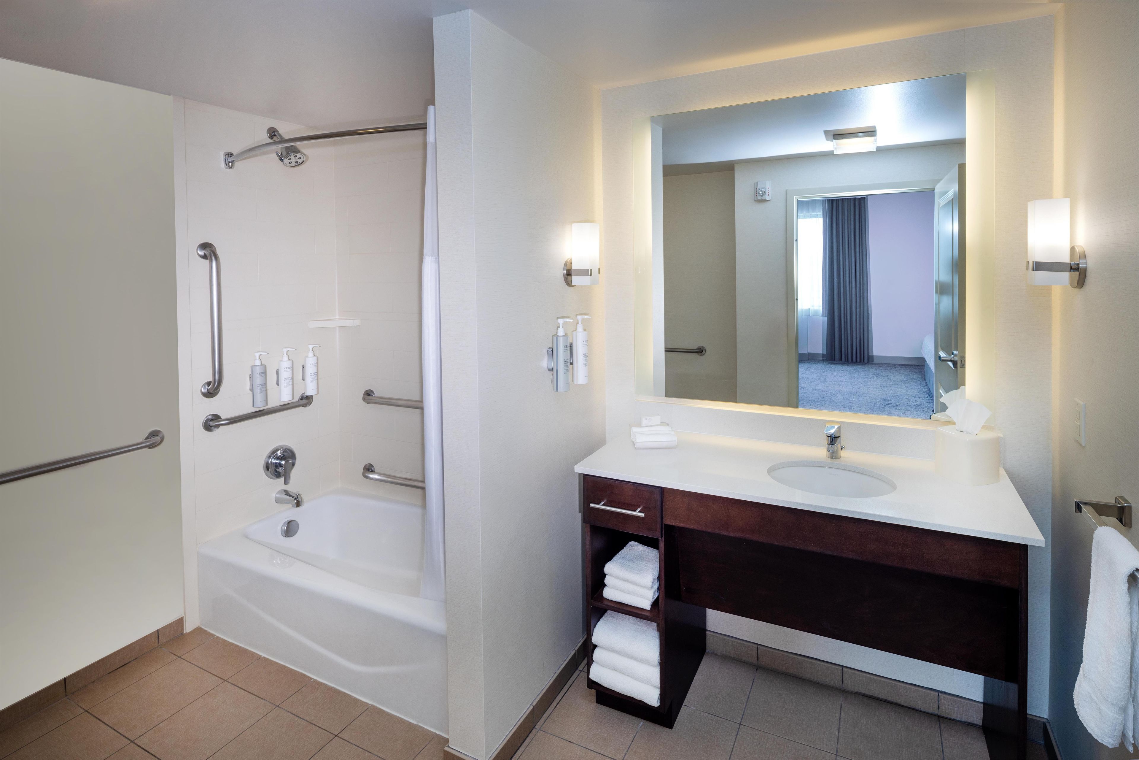 A modern bathroom with a bathtub, a vanity with a mirror, and a towel rack.