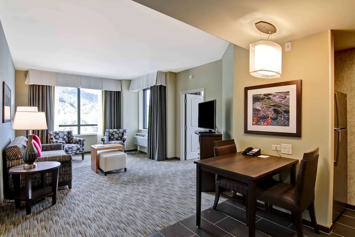 A hotel room with a dining area, a sofa, a TV, and a painting on the wall.