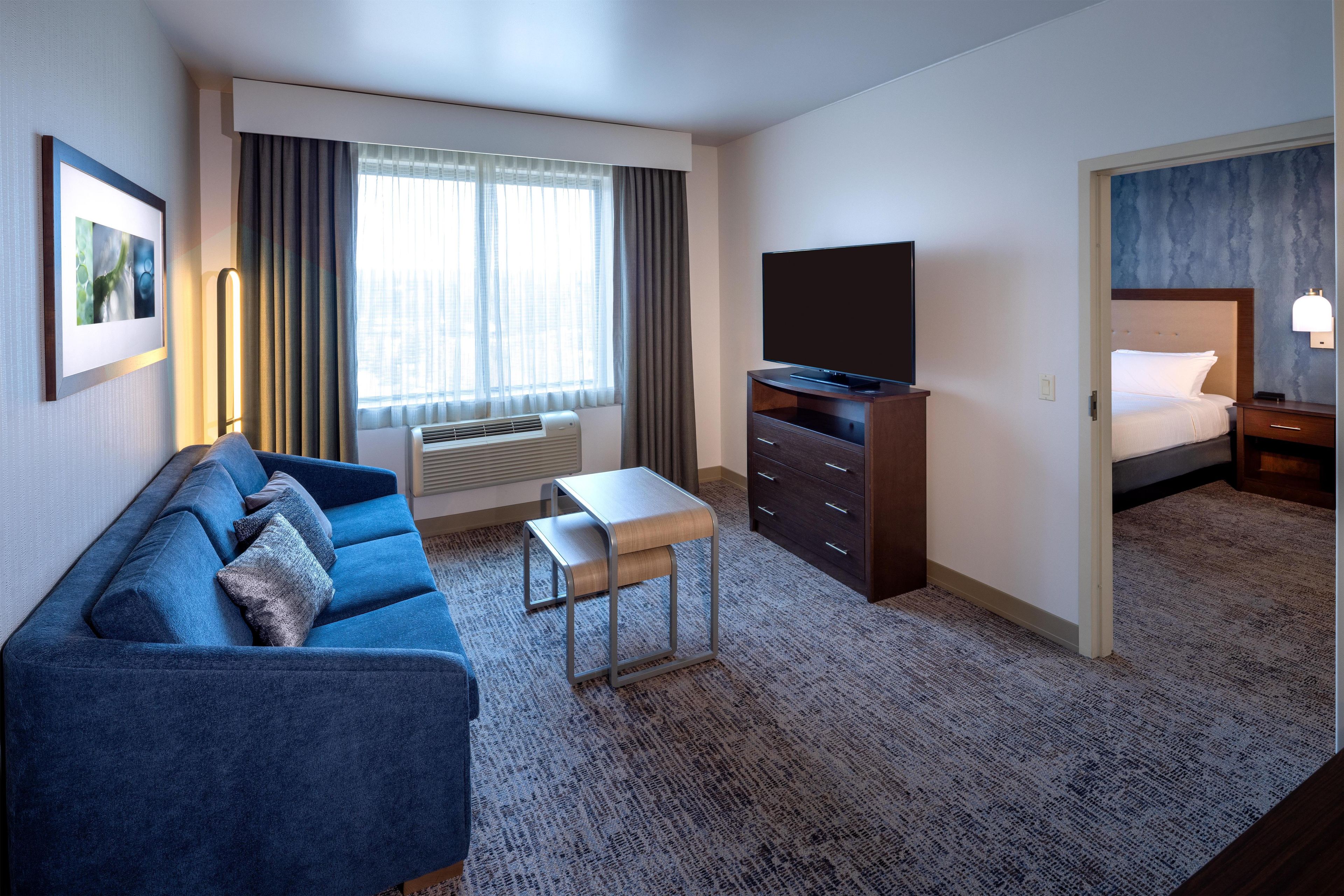 A hotel room with a blue sofa, a flat-screen TV, a dresser, and a bed.