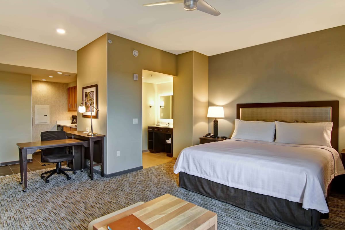 A hotel room with a bed, desk, chair, and a small table.