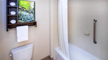 A bathroom with a toilet, a shower with a grab bar, and a shelf with towels and a painting.