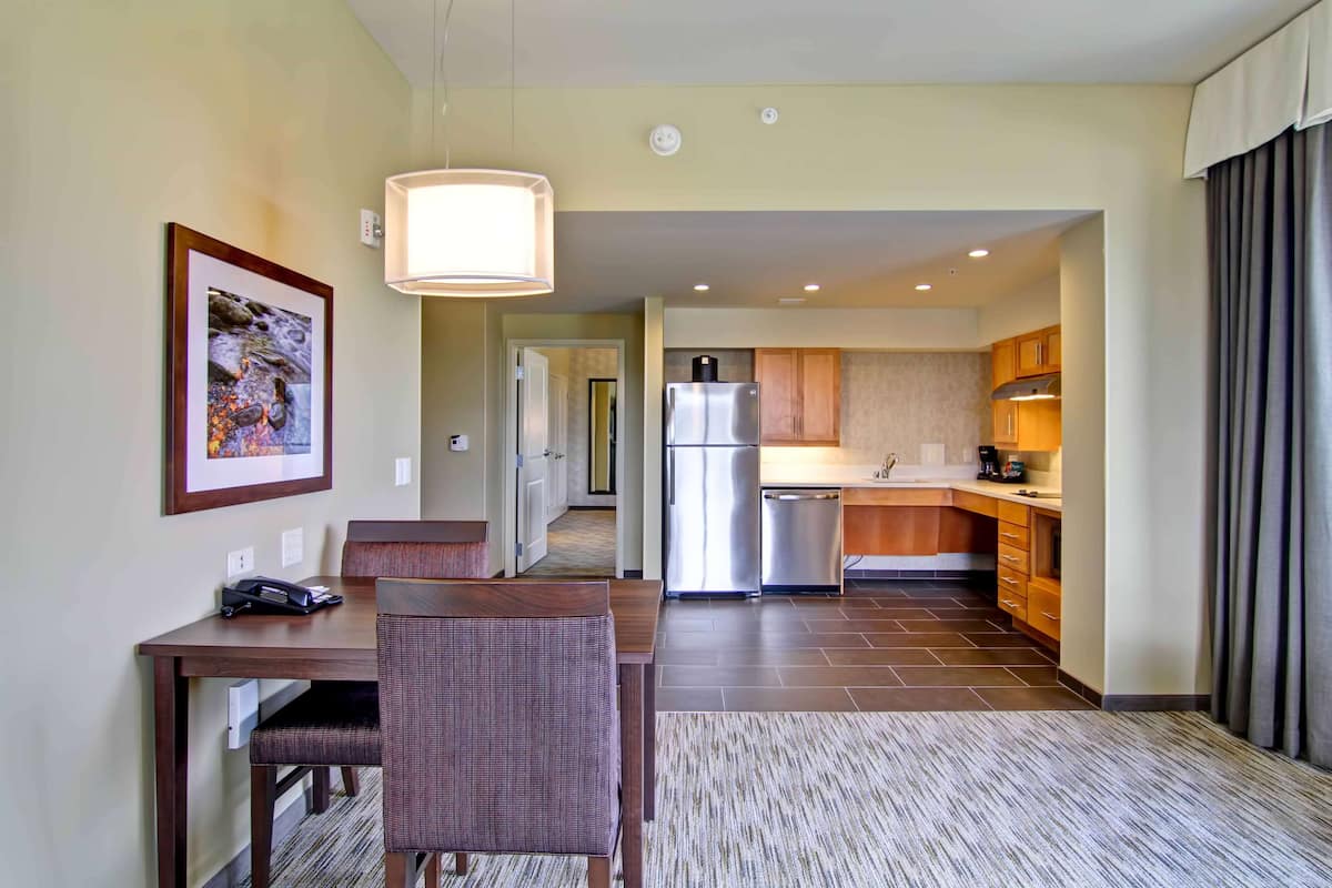 A modern hotel room with a dining area, kitchenette, and a framed picture on the wall.