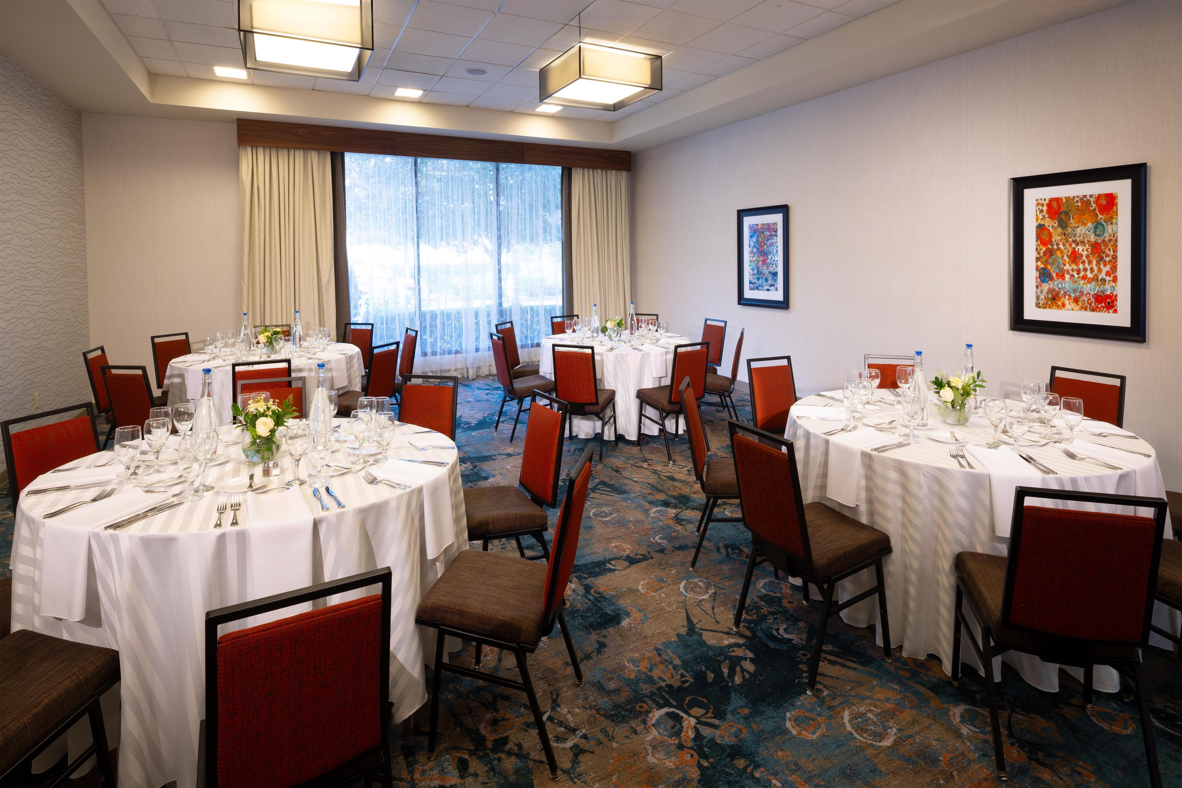 A conference room with multiple round tables set for dining, equipped with chairs and table settings.