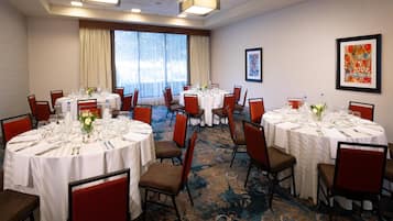 A conference room with multiple round tables set for dining, equipped with chairs and table settings.
