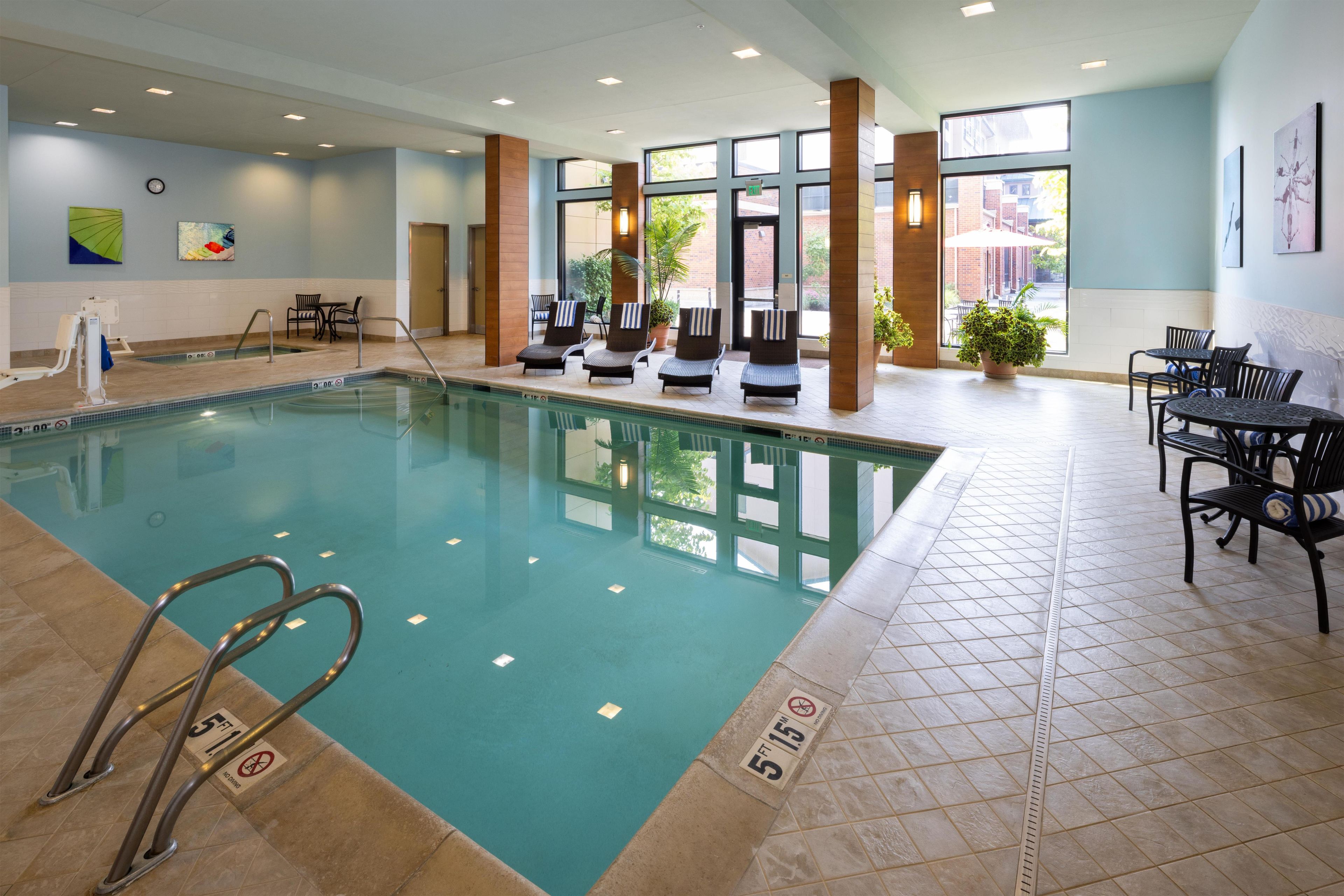 An indoor swimming pool with lounge chairs, a table, and chairs.
