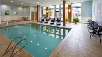 An indoor swimming pool with lounge chairs, a table, and chairs.