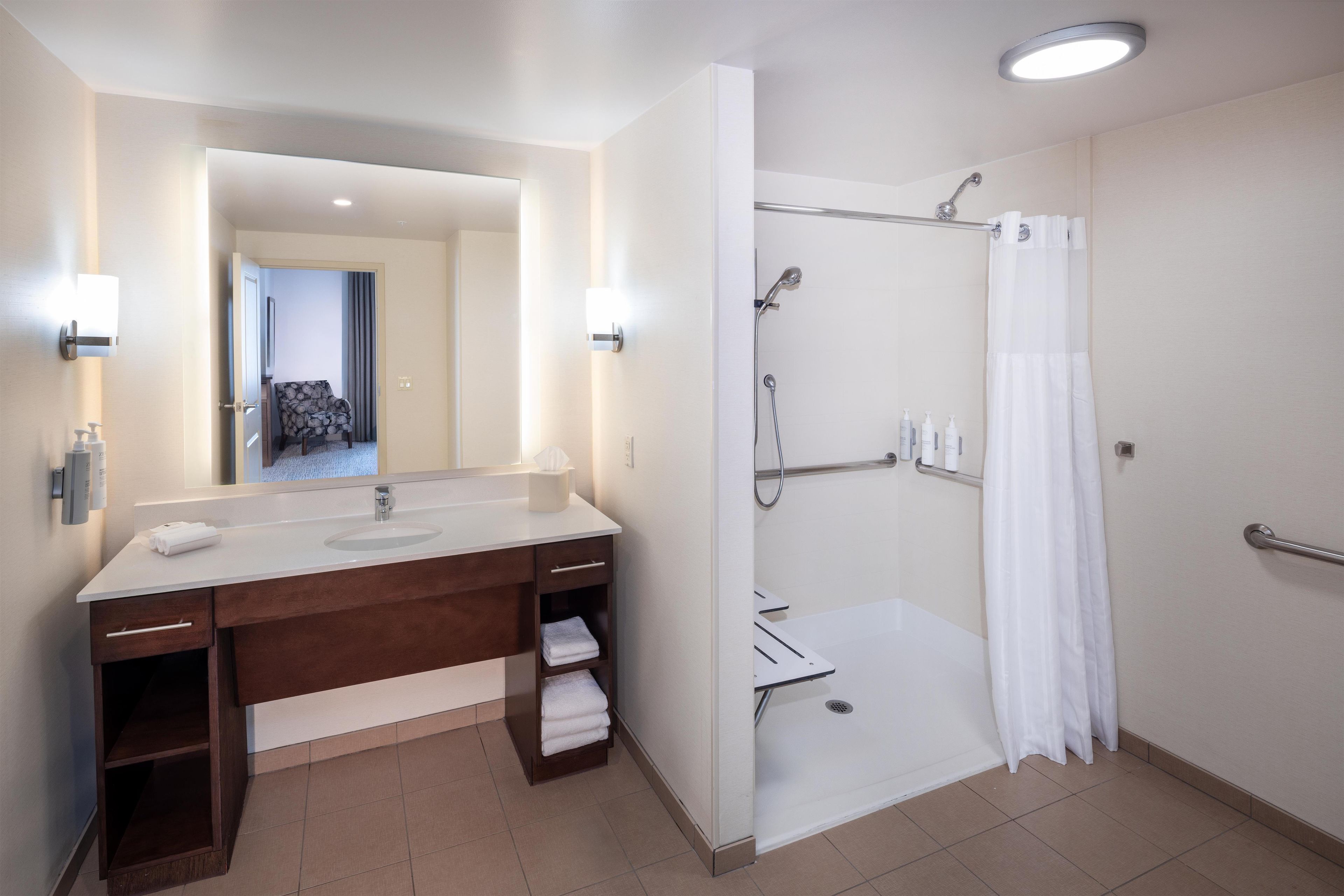 A modern bathroom with a dual sink vanity, a shower with a glass door, and a visible toilet in the background.