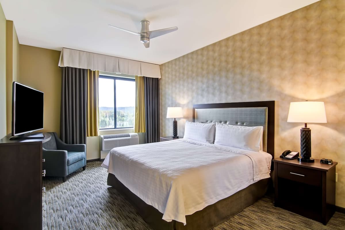 A hotel room with a bed, a desk with a TV, a chair, two bedside lamps, and a window with curtains.