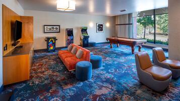 A hotel room with a pool table, a sofa, a television, arcade games, and a large window with a view.