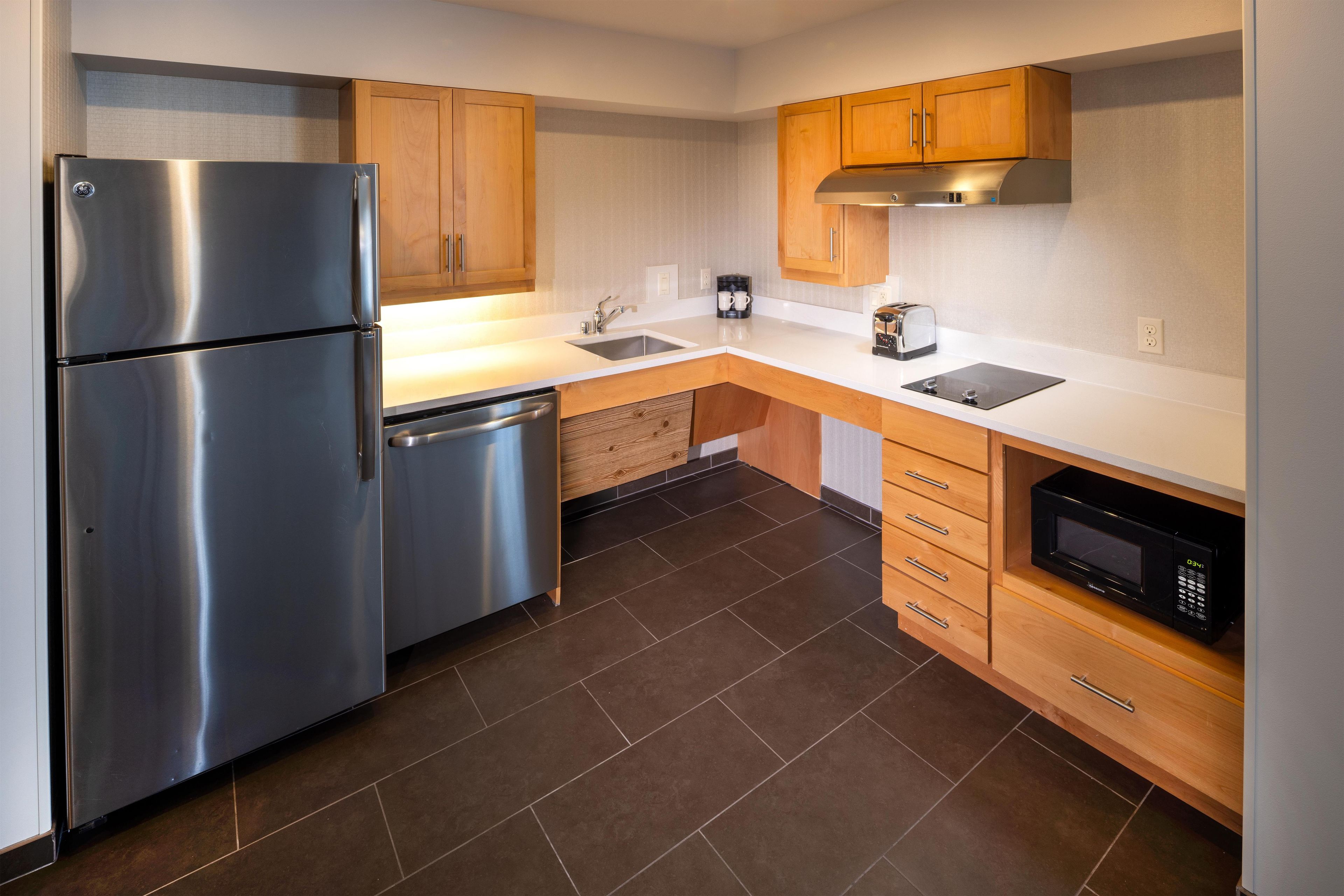 A modern kitchen with stainless steel appliances, wooden cabinets, and a black microwave.