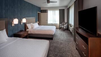 A hotel room with two beds, a TV, a ceiling fan, and a large window with curtains.