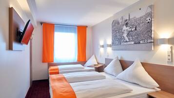 Habitación de hotel con dos camas, un televisor montado en la pared, un ventanal grande con cortinas anaranjadas y una obra de arte con temática deportiva.