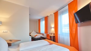 A hotel room with a bed, a desk, a chair, a TV, and a window with curtains.