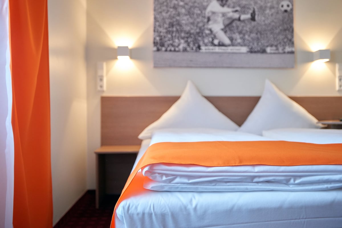 A hotel room with a neatly made bed, a nightstand, and a wall-mounted picture.