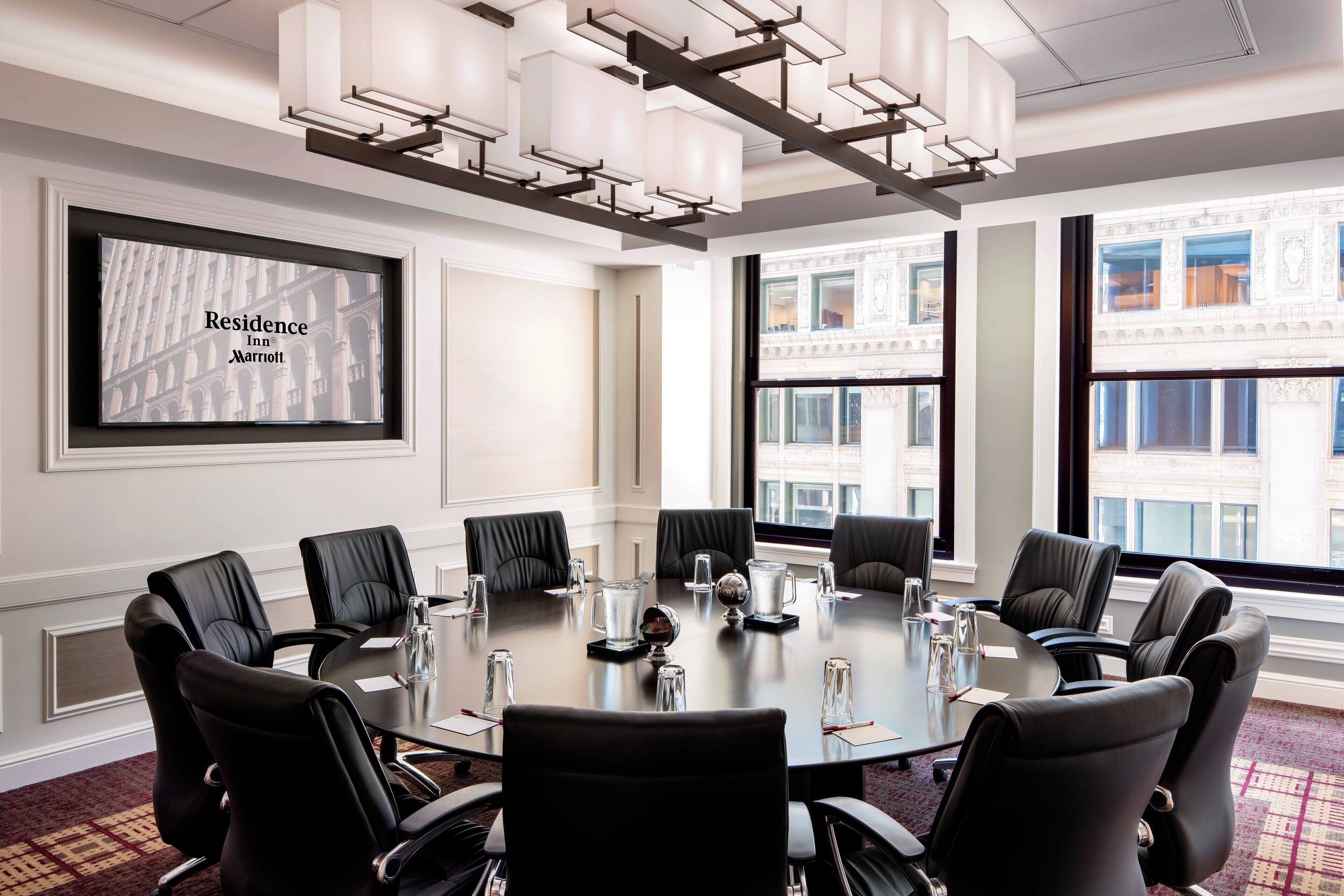 A conference room with a large table, black leather chairs, and a screen displaying "Residence Inn Marriott".